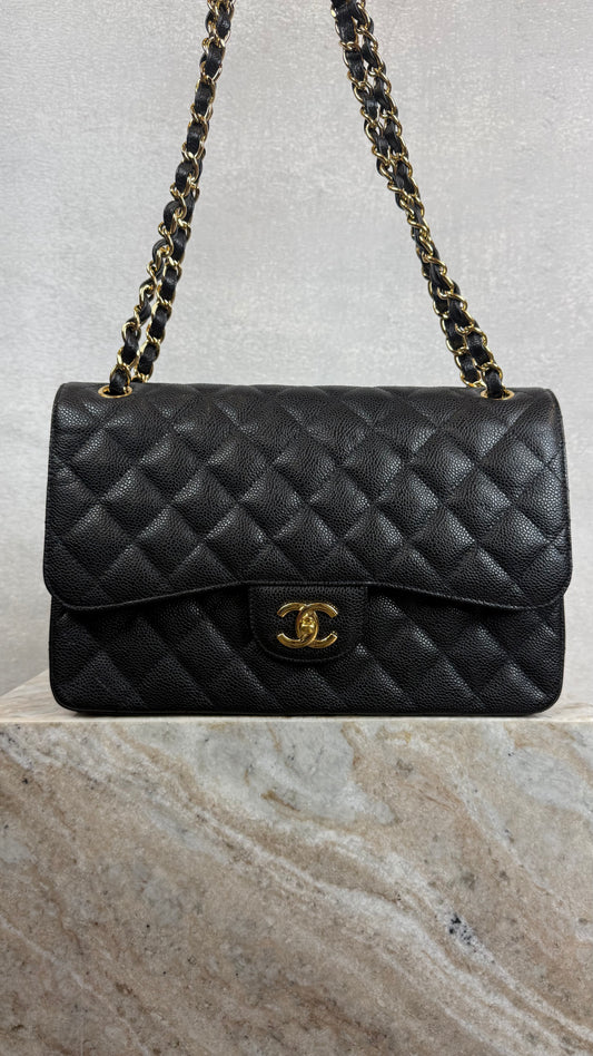 Black quilted handbag with gold chain strap on a marble surface