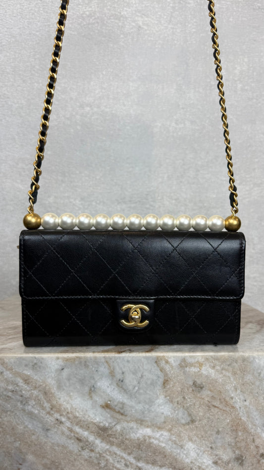 Black quilted chanel handbag with pearl embellishments and gold chain on a light gray background